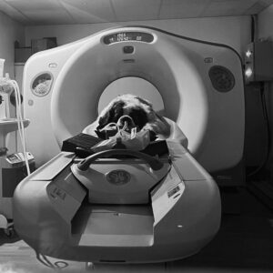 A dog lies calmly inside a CT scanner, with its head placed in the machine, as three RCVS Advanced Practitioners supervise the procedure in this veterinary medical environment.