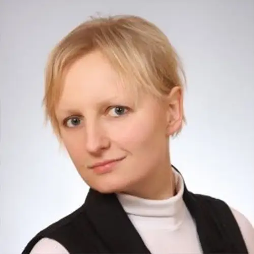 A person with short blonde hair, dressed in a white polo neck and a black waistcoat, radiates the composed professionalism of veterinary specialists against an unadorned background.