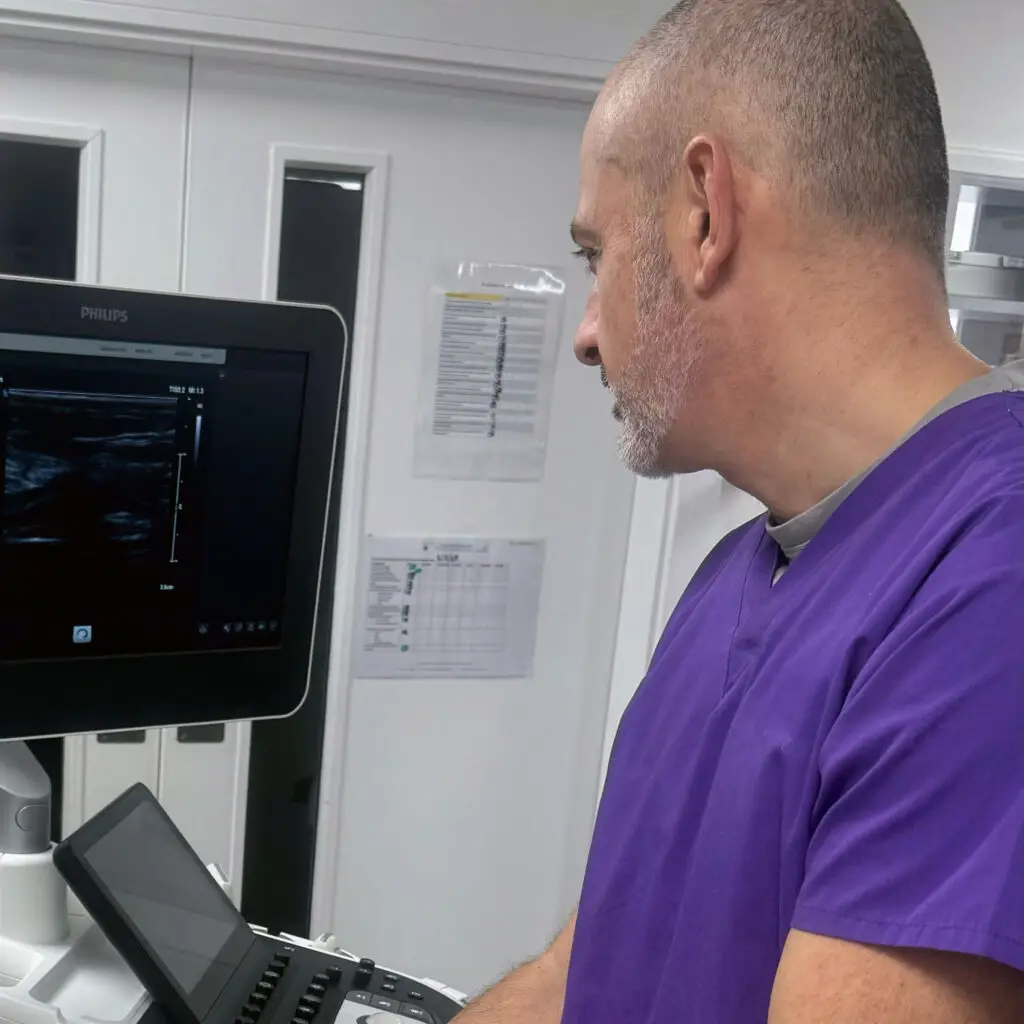 In a veterinary referral environment, a man wearing purple scrubs, one of three RCVS Advanced Practitioners, skilfully operates an ultrasound machine.